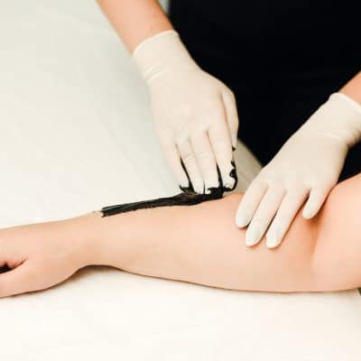 A beautician makes hair removal for clean, beautiful skin without hair. Depilation with black wax.